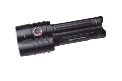 Fenix LR35R rechargeable LED flashlight with 10,000 lumens, black body, turned on beam illuminating a dark area.