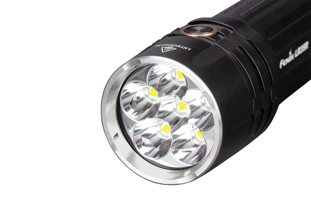 Fenix LR35R rechargeable LED flashlight with 10,000 lumens, black body, and adjustable focus, shown turned on in a dark setting.